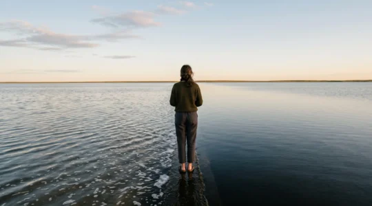 Une personne debout à la limite entre une eau calme et une eau agitée, symbolisant l'équilibre émotionnel entre étouffer et laisser exploser ses émotions